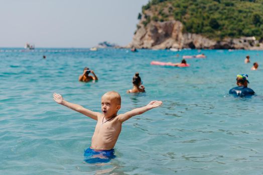 Child learning to swim in the open sea of tropical resort. Kids learn swimming. Exercise and training for young children. Little boy with colorful float board in sport club. Swimming baby or toddler. Happy child boy swims in sea in swimming circle with splash. Blue sky and water. Swimming training. Fun joy activities on vacation in the beach. Childhood moments lifestyle. Freedom careless. boy swim in the sea.