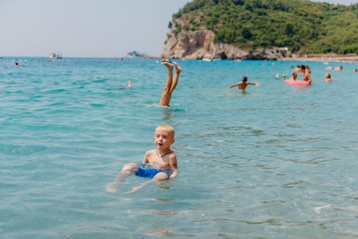 Child learning to swim in the open sea of tropical resort. Kids learn swimming. Exercise and training for young children. Little boy with colorful float board in sport club. Swimming baby or toddler. Happy child boy swims in sea in swimming circle with splash. Blue sky and water. Swimming training. Fun joy activities on vacation in the beach. Childhood moments lifestyle. Freedom careless. boy swim in the sea.