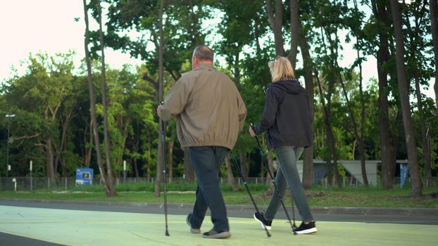 Pensioners are engaged in Nordic walking in the park. A man and a woman walk with sticks to improve health. 4k