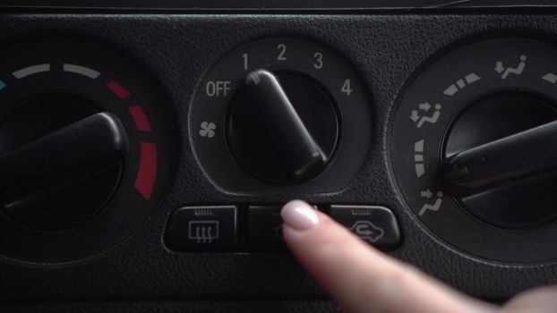 The woman turns on the fan and presses the air conditioner button in the car. Automotive panel close-up. 4k