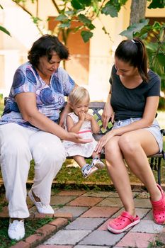 Mom, grandmother and little girl sit on a bench in the park. High quality photo