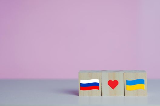 Wooden cubes with russia flag symbol and ukraine flag with red heart icon on background.