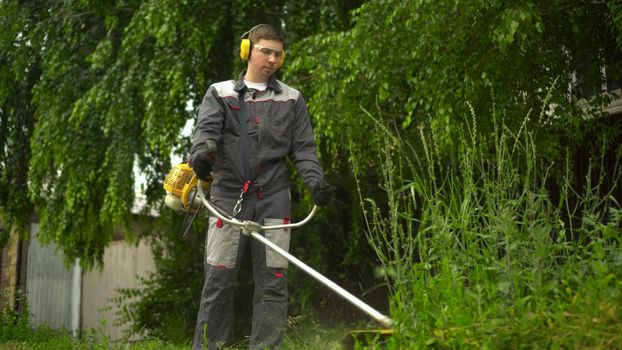 A young man from the special services mows the lawn with a petrol trimmer. A man in glasses and headphones with a lawn mower in his hands. 4k