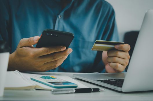 man hand holding credit card and mobile phone online shopping e-commerce and internet banking at desk.