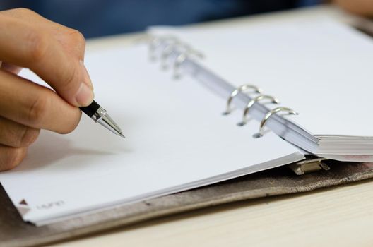 close up holding a pen and writing at the notebook.