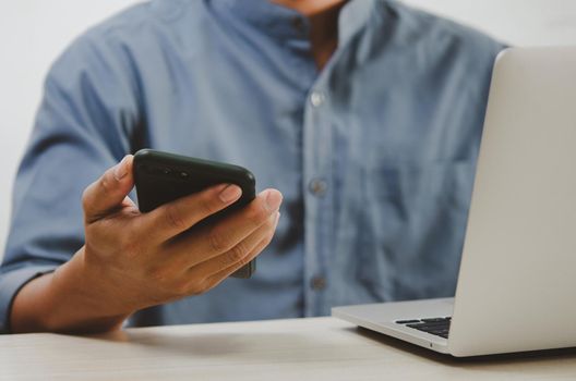 man using mobile smart phone and computer laptop searching internet, sending sms, using text messenger or online banking.