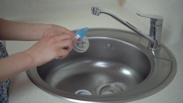 A young mother cleans the nipple from a baby food bottle with a special brush. Close-up hands. 4k