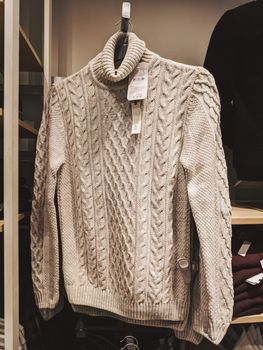 Beige knitted sweater with a neck on a hanger in a store. High quality photo