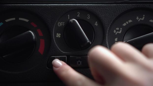 The woman turns on the fan and presses the window heating button in the car. Automotive panel close-up. 4k