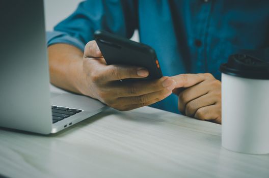 man hand holding smartphone and computer laptop to working technology searching internet, sending sms, using text messenger or online banking.