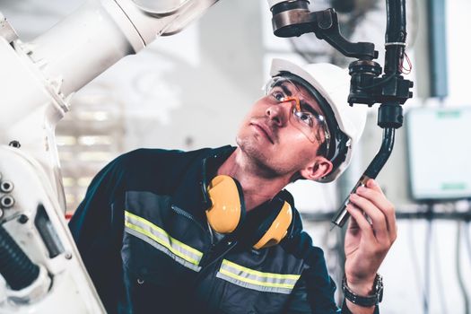 Young factory worker working with adept robotic arm in a workshop . Industry robot programming software for automated manufacturing technology .