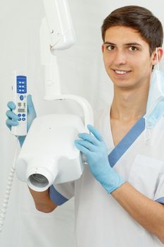 Portrait of handsome male dentist with dental x-ray machine in the dental clinic. Doctor wearing white uniform and blue gloves