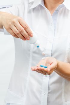 Female doctor holding a jar and offering pills. The tablets fall out of the bottle. Selective focus on pills
