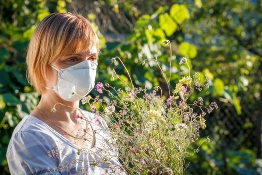 Unhappy woman in protection mask holding bouquet of wildflowers and trying to fight allergies to pollen. Woman protecting her nose from allergens. Allergy concept.