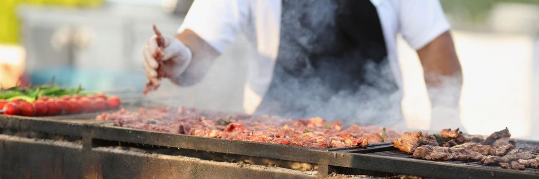 Close-up of professional male chef frying fresh meat on grill on open air. Man cook meal for visitors. Food, cafe, barbeque, cook, street kitchen concept