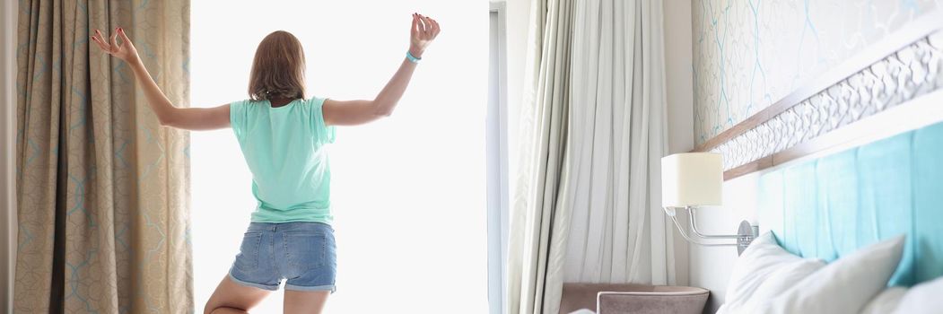 Portrait of woman doing yoga near light window in bedroom with stylish interior. Female stand in position on one leg and meditate. Habit, morning concept