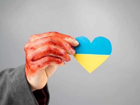 Woman with hands covered in blood holding a heart with the flag of ukraine on a white background