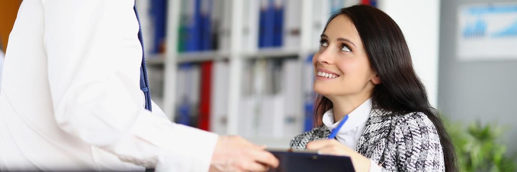 Portrait of smiling business woman signing document, employee give agreement paper to boss lady. Stylish suit on woman worker, office interior. Job concept