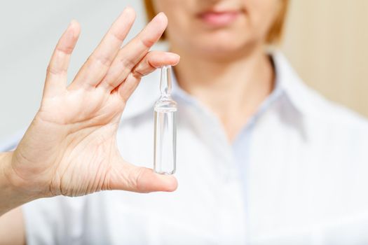 Hand of female doctor with ampoule and medicine. Selective focus on ampoule