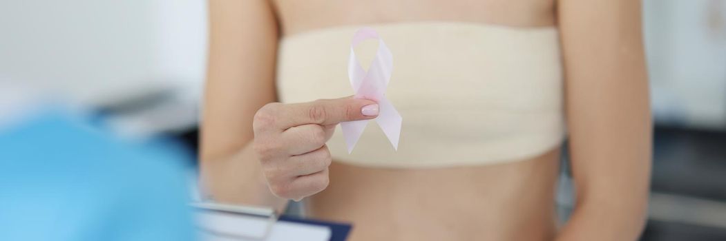 Close-up of female client hold white ribbon sign of breast cancer. Patient on doctor consultation in hospital. Clinic, medicine, treatment, illness concept