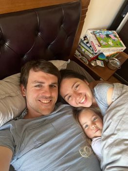 Smiling mom, dad and little daughter lie in bed under the covers. High quality photo