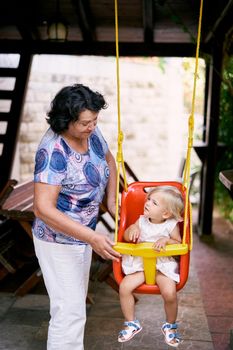 Grandmother shakes the girl on a swing in a wooden gazebo. High quality photo