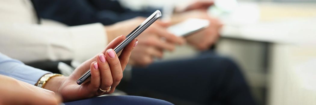 Close-up of female hands with manicure hold mobile phone device. Manager in conference room have discussion about business project. Company meeting concept