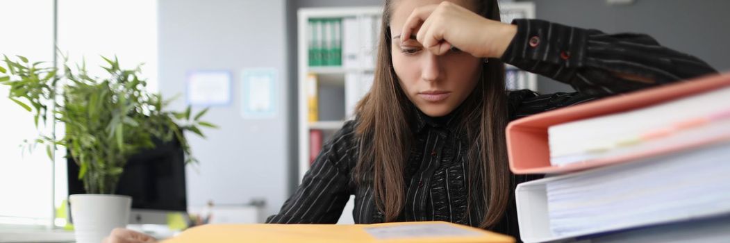 Portrait of tired overworked woman with hopeless look on docs pile. Stressful and exhausted clerk in office, stack with papers on desk. Hardworker concept