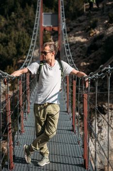 Man hiking in the mountains with backpack, standing on the bridge on sunny day