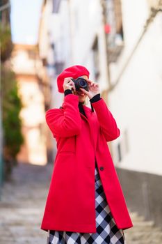 From below of positive young female traveler with blond hair in stylish outfit smiling while taking photos standing on aged narrow stairway during trip