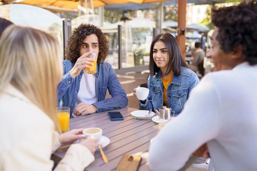 Multi-ethnic group of friends having a drink together in an outdoor bar. Young people having fun.