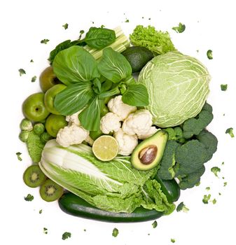 Bunch of greens and herbs laid on white countertop. Halved avocado, lettuce salad leaves, raw broccoli and other vegetables in row. Vegan diet concept.