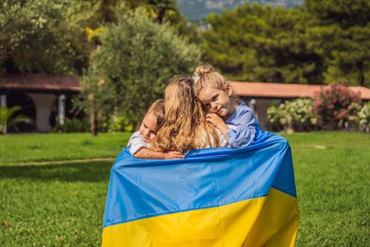 Ukrainian mother with two children with flag of Ukraine. Outside. Concept of problem of war in Europe, supporting of families and children, migrants, emigration, patriotism, motherhood, Ukrainian women.