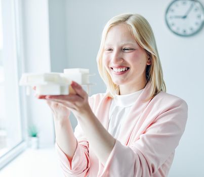 portrait of a young business woman holding a modern house model in the office