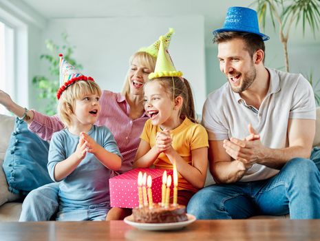 Family of four, mother, father, daughter and son having fun celebrating a birthday together with birthday cake and candles and a present at home