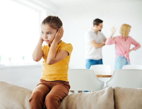 Portrait of a sad child, a little girl, while parents are having an argument at home