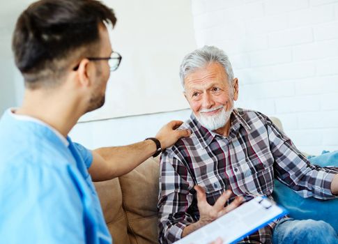 Doctor or nurse caregiver talking with senior man on sofa at home or nursing home