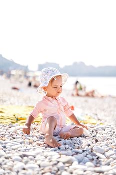 Little girl in a panama hat sits on a pebble beach. High quality photo