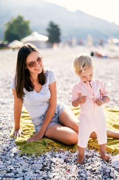 Little girl unzips a child suit while standing on the beach. High quality photo