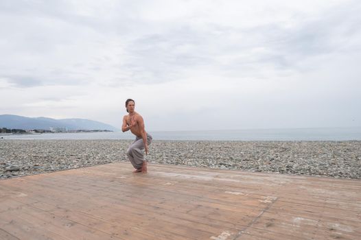 Caucasian man with naked torso practicing wushu on the seashore