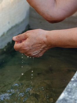 Woman watering and washing on a public foutain in Castell'Arquato Italy.Pure and precious to nature. Shot of hands held out to catch a stream of water outside.