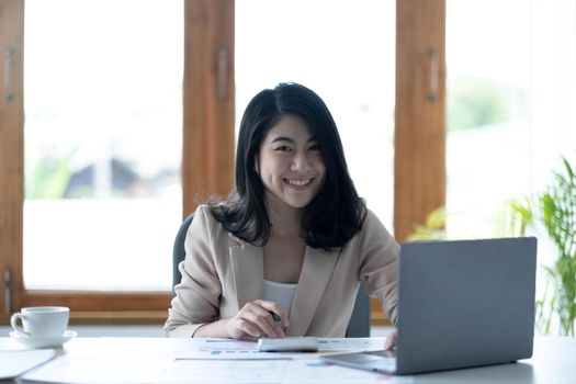 Charming Asian woman working at the office using a laptop Looking at the camera..