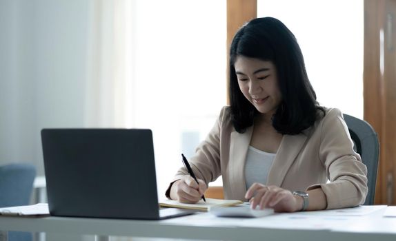 Beautiful Asian businesswoman analyzes charts using laptop calculator at the office..