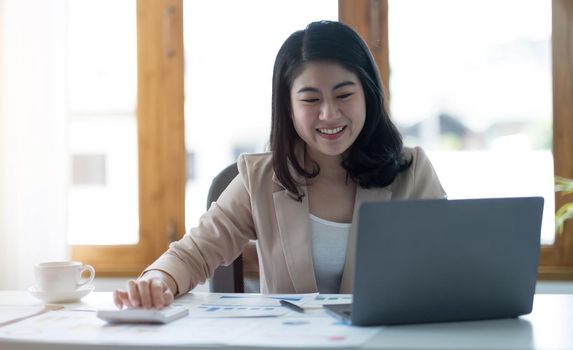 Beautiful young asian woman sitting at coffee shop using laptop. Happy young businesswoman sitting at table in cafe with tab top computer..