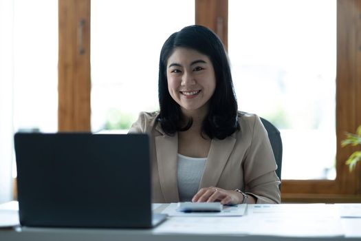 Charming Asian woman working at the office using a laptop Looking at the camera..