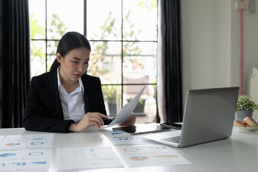 Female businesswoman readind financial report analyzing statistics pointing at pie chart working at her desk.