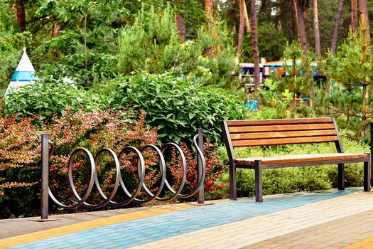 a large public green area in a town, used for recreation. Wooden bench and bike rack in a green city park with rides and trees