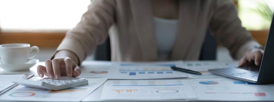 Close up Business woman using calculator and laptop for do math finance on wooden desk in office and business working background, tax, accounting, statistics and analytic research concept.