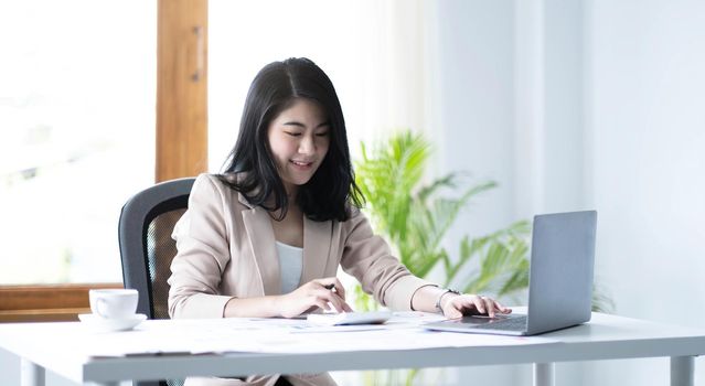 Beautiful Asian businesswoman analyzes charts using laptop calculator at the office..