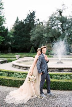 Bride with a bouquet hugs the groom from behind near the fountain. High quality photo